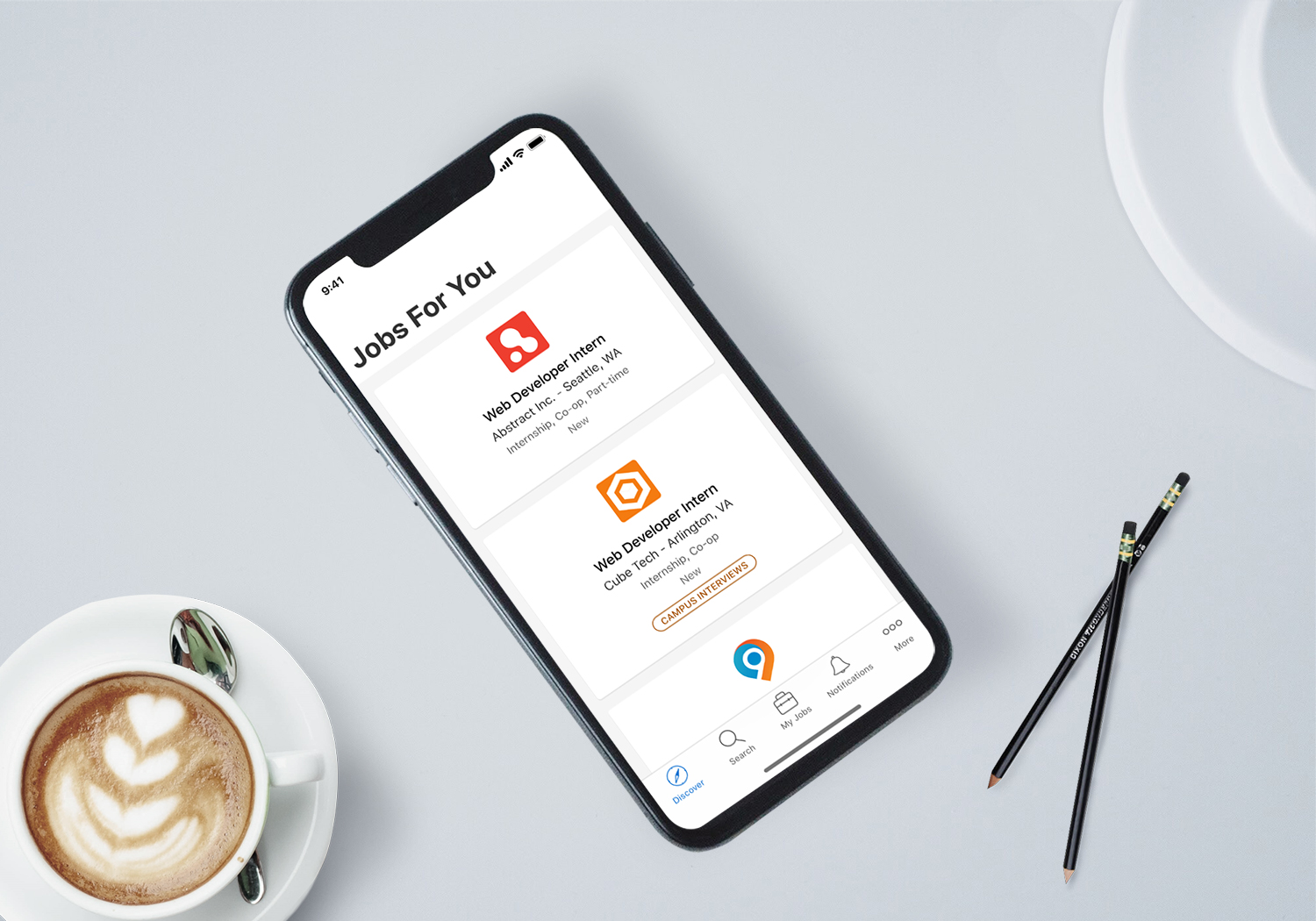 iPhone displaying the Symplicity Jobs For You screen with job listings, alongside a coffee cup and pencils